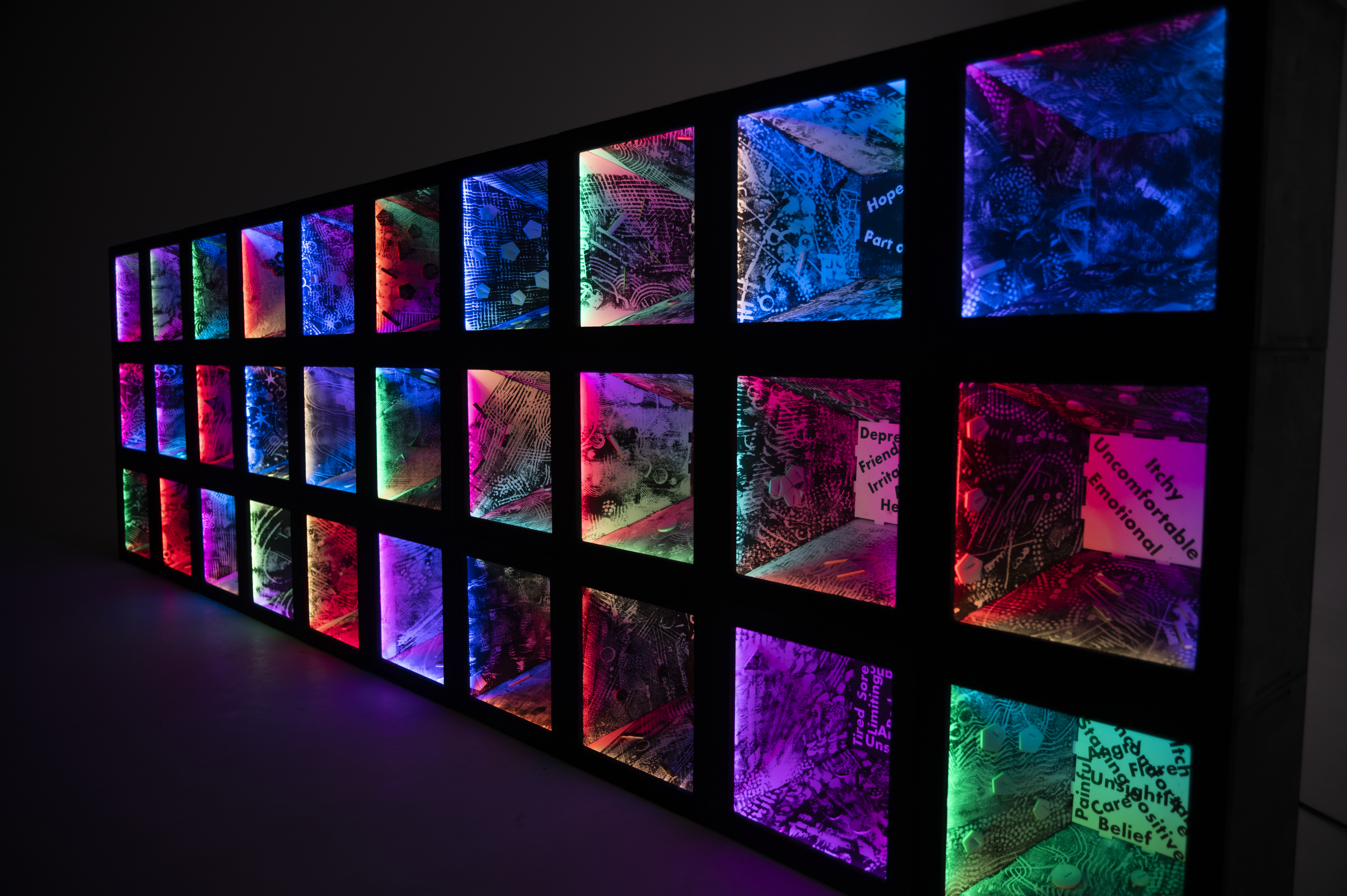Sculpture created by Julia Vogl and Peter Hudson, in collaboration with participants of the &#039;Colouring Adult Eczema&#039; project. 30 illuminated boxes, lit in different colours and marked with various patterns are stacked on each other to form a wall.