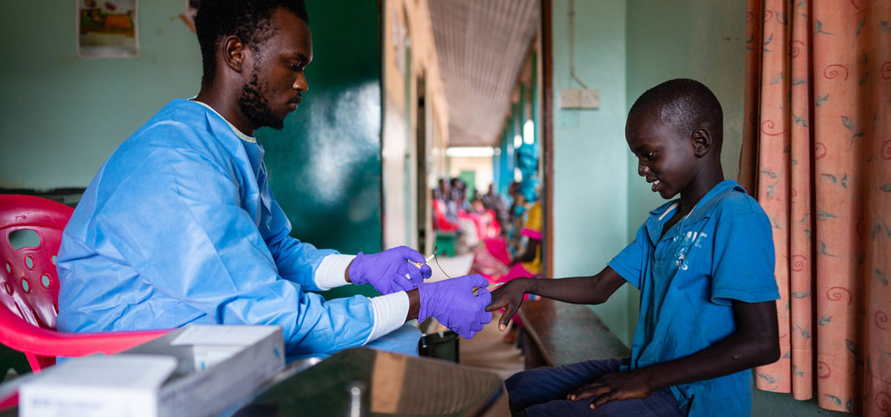 A clinician taking a blood sample from a young boy in Sibanor, Gambia