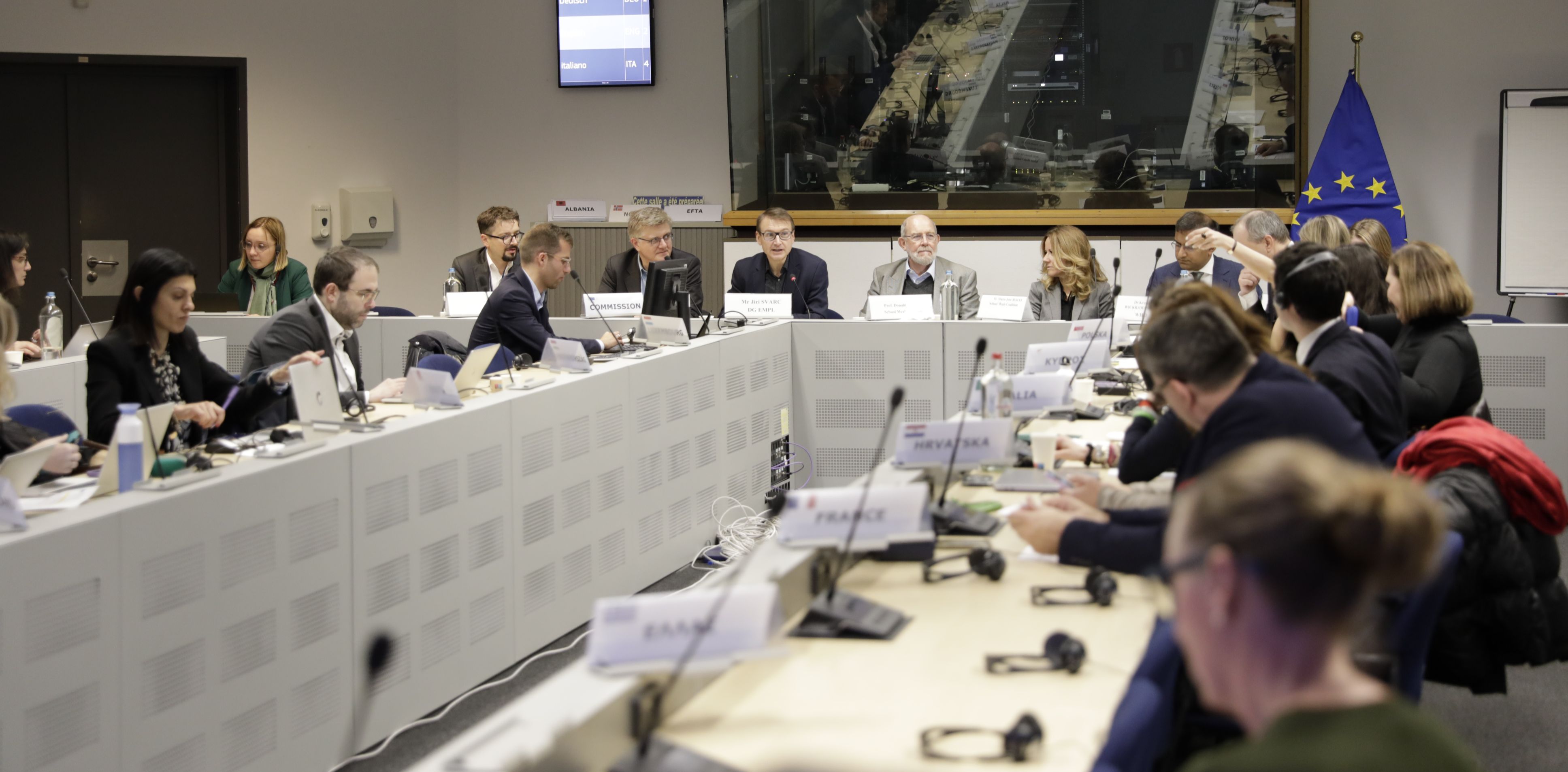 A group of men and women in suits are seated at a U-shaped conference table