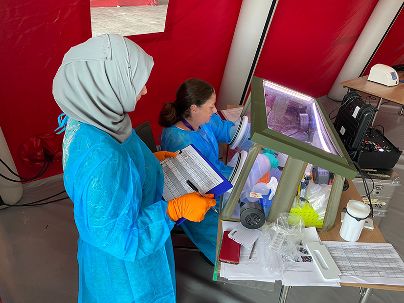 UK-PHRST microbiology team in rapid response mobile lab tent operating equipment with colleague standing over observing
