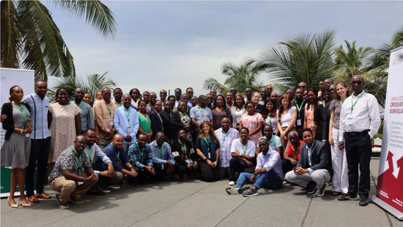 Group photo of participants in RCCE Kenya Cross-border exercise standing infront of outside backdrop with palm trees