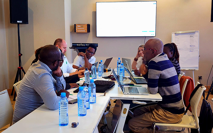 Members of UK-PHRST Research team sitting around meeting table with KEMRI-Wellcome Trust colleagues discussing research project.