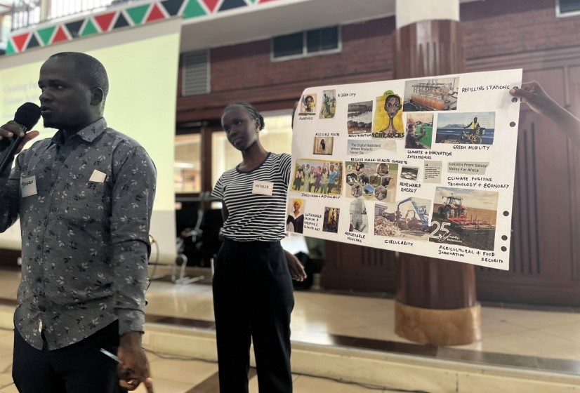 A black man stands on the left with a microphone speaking, while behind him a black woman holds up a poster with different images on depicting their future visions for a green city