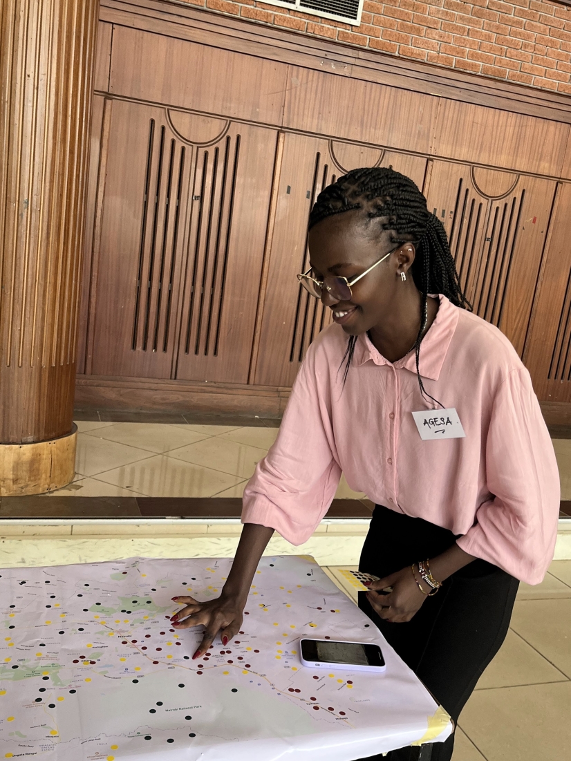 Black woman wearing a pink shirt smiling with her hand putting a sticker on a map laid on a table