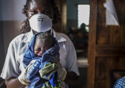 A nurse with face mask holding a newborn baby