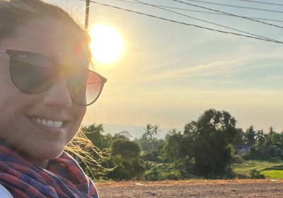 The student smiling while driving a motorbike in front of sunset