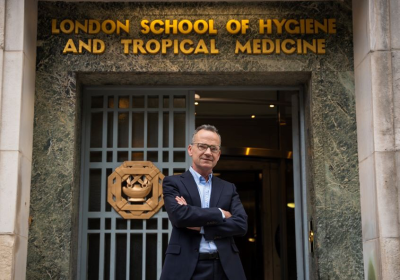 Liam Smeeth in a dark suit stood with arms folded outside the entrance to LSHTM&#039;s Keppel Street building