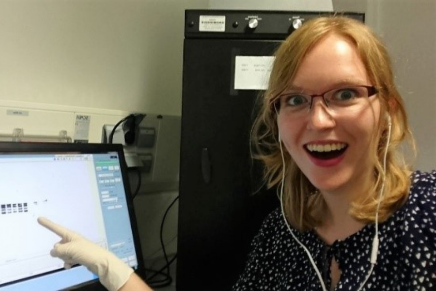 Alica is smiling to camera and pointing to a computer screen showing some lab results