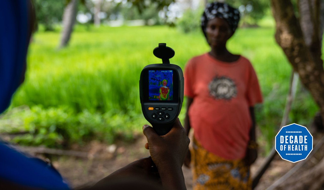 A field worker from MRC Unit The Gambia at LSHTM uses a thermal imaging camera to measure a mother and her unborn baby&#039;s temperature in Keneba as part of a study looking at the impact of heat stress on pregnant farmers. Credit: Louis Leeson/LSHTM